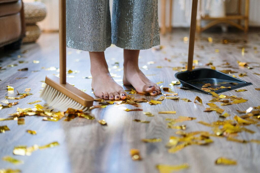 Housemate's feet with broom and pan surrounded by party mess