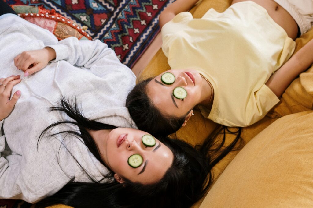 Two Women Lying Down On Sofa With Cucumbers over their Eyes